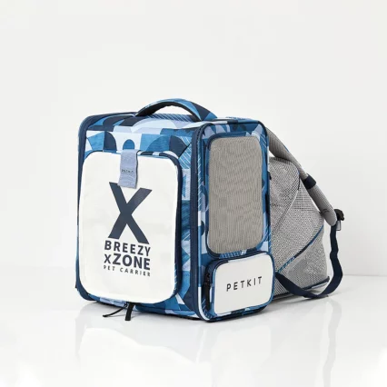 Šioje nuotraukoje matoma „Petkit Breezy X-Zone“ gyvūnų transportavimo kuprinė. Ji yra marginta įvairių atspalvių mėlyna ir balta spalvomis, primenančiomis geometrinius raštus. Kuprinės priekyje yra didelė balta kišenė su juodu stilizuotu „X“ formos logotipu ir užrašu „BREEZY XZONE PET CARRIER“ po juo. Viršuje, centre, yra šviesiai mėlyna etiketė su baltu užrašu „PETKIT“. Kuprinė turi juodą rankeną viršuje ir dvi reguliuojamas petnešas nugaroje. Priekinės kišenės apačioje matomi du juodi raišteliai. Šone yra kišenė su baltu fonu ir mėlynu užrašu „PETKIT“. Kuprinė stovi ant blizgaus balto paviršiaus, atspindinčio jos apačią. Fonas yra šviesiai pilkas.