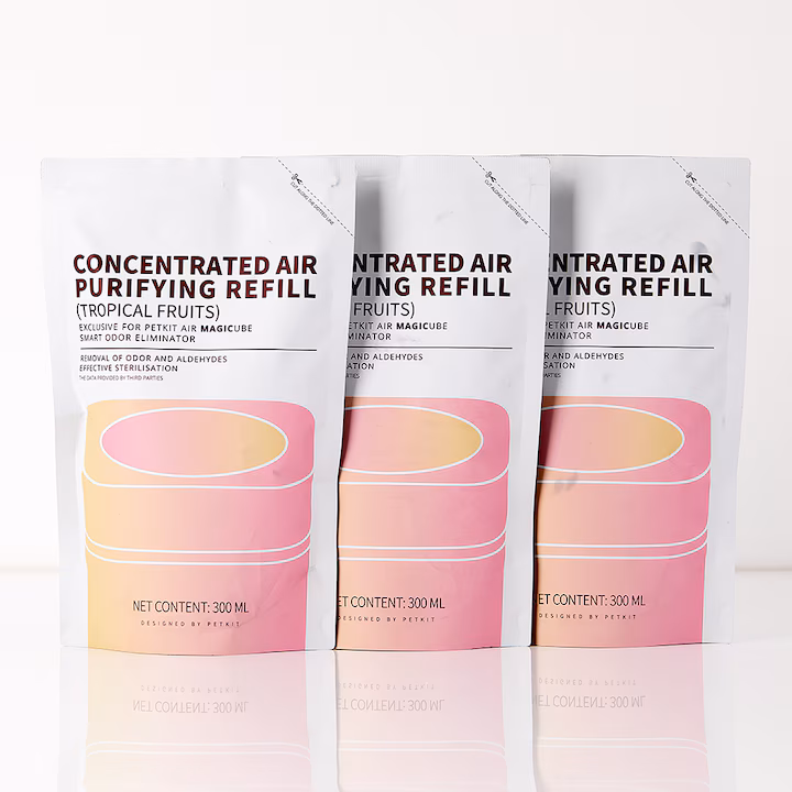 Kiekvieno maišelio viršuje yra violetinis tekstas: "CONCENTRATED AIR PURIFYING REFILL" (Koncentruotas oro valymo papildymas), o po jo skliausteliuose "(TROPICAL FRUITS)" (Tropiniai vaisiai). Žemiau, smulkesniu violetiniu šriftu, rašoma: "EXCLUSIVE FOR PETKIT AIR MAGICUBE SMART ODOR ELIMINATOR" (Skirtas PETKIT Air Magicube išmaniajam kvapų naikintojui), "REMOVAL OF ODOR AND ALDEHYDES" (Pašalina kvapus ir aldehidus) ir "EFFECTIVE STERILISATION" (Efektyvi sterilizacija). Kiekviename maišelyje taip pat pavaizduotas PETKIT Air Magicube įrenginio grafinis atvaizdas su rožiniu ir geltonu pereinamuoju fonu. Kiekvieno maišelio apačioje, smulkesniu rožiniu šriftu, nurodyta "NET CONTENT: 300 ML" (Grynasis kiekis: 300 ml). Kiekvienas maišelis turi įpjovą viršuje patogiam atidarymui.